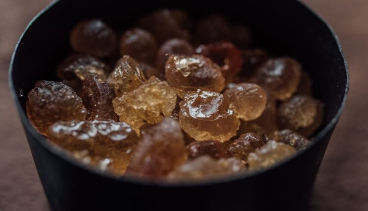 A detailed close-up of brown rock mastic crystals inside a black container, showcasing texture and color contrast.