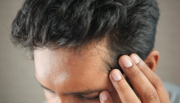 Close-up of a man's hand touching his head in contemplation. Neutral tones and soft lighting.
