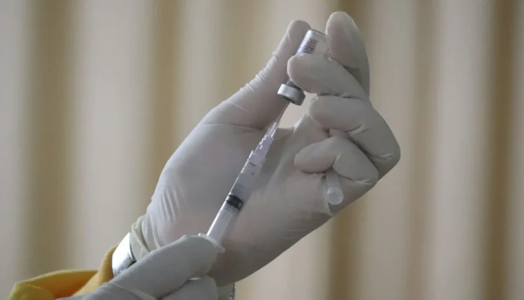 A person in white latex gloves drawing liquid from a vial into a syringe