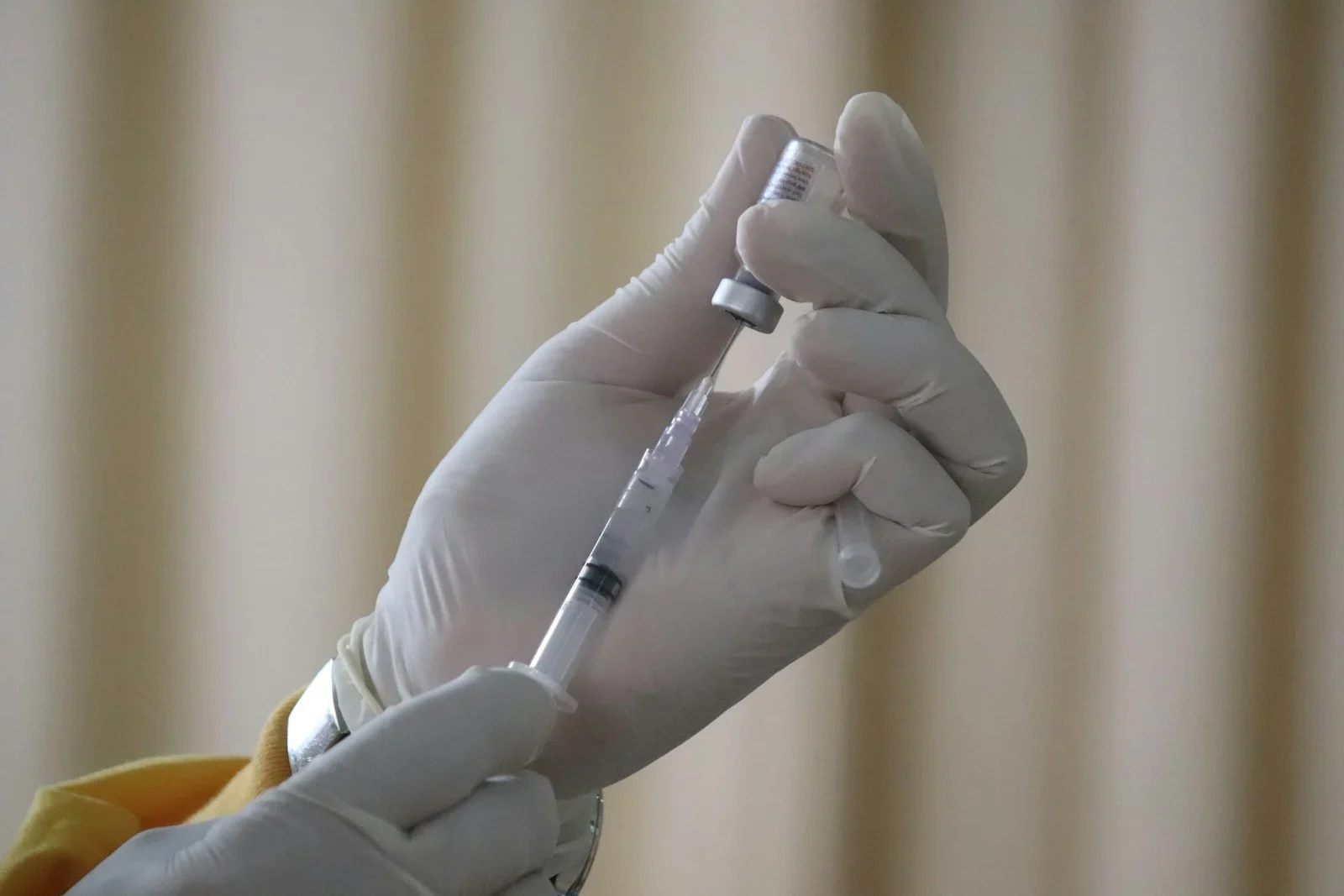 A person in white latex gloves drawing liquid from a vial into a syringe