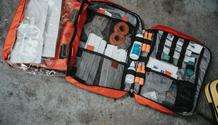 An open red medical bag filled with various supplies on a grey surface