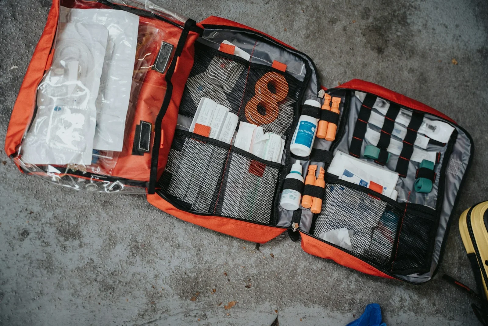 An open red medical bag filled with various supplies on a grey surface