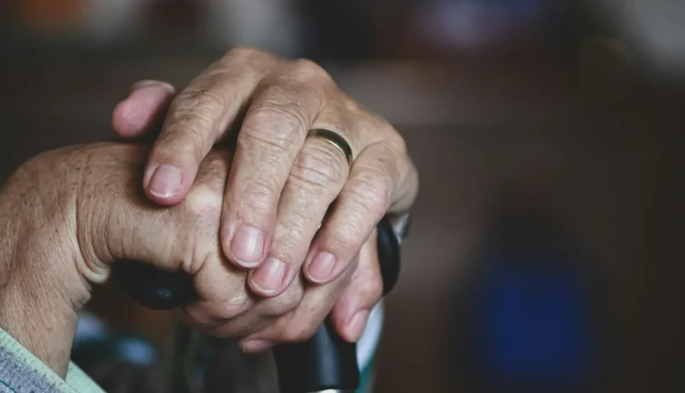 Wrinkled hands with a gold ring resting on a black cane handle