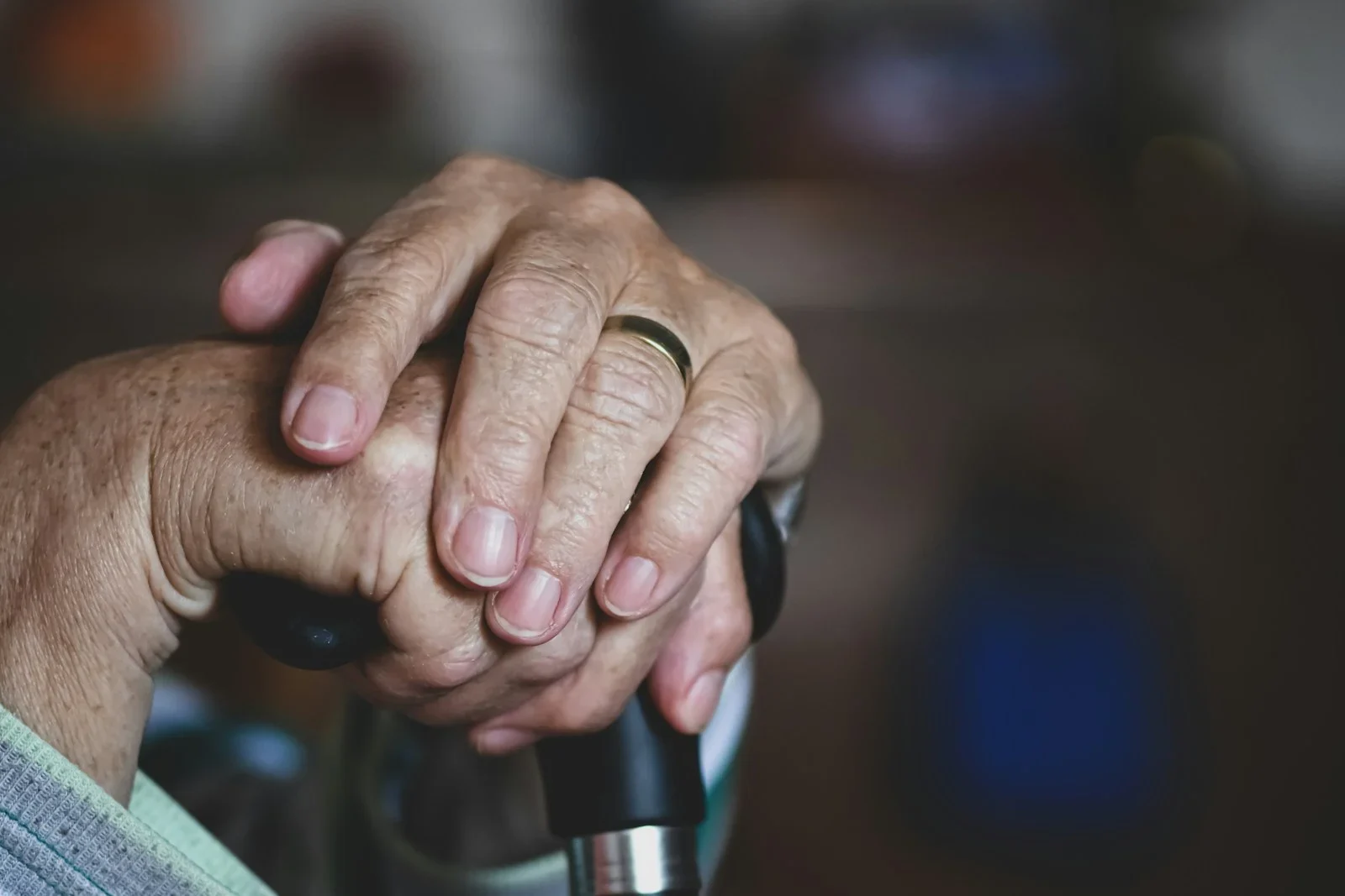Wrinkled hands with a gold ring resting on a black cane handle